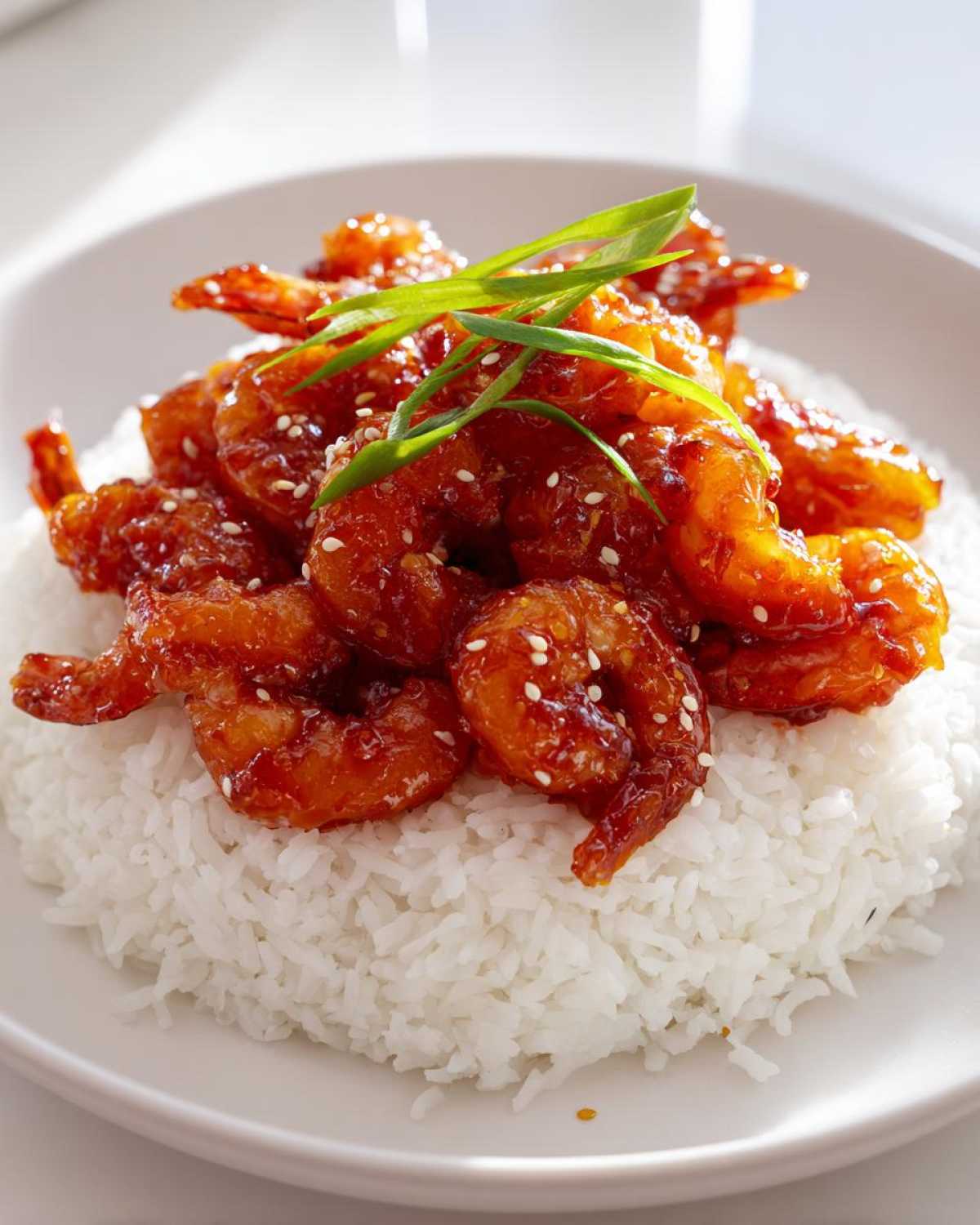 Close-up of Sticky Sweet Chili Shrimp piled on a bed of fluffy white rice, garnished with sesame seeds and green onions.