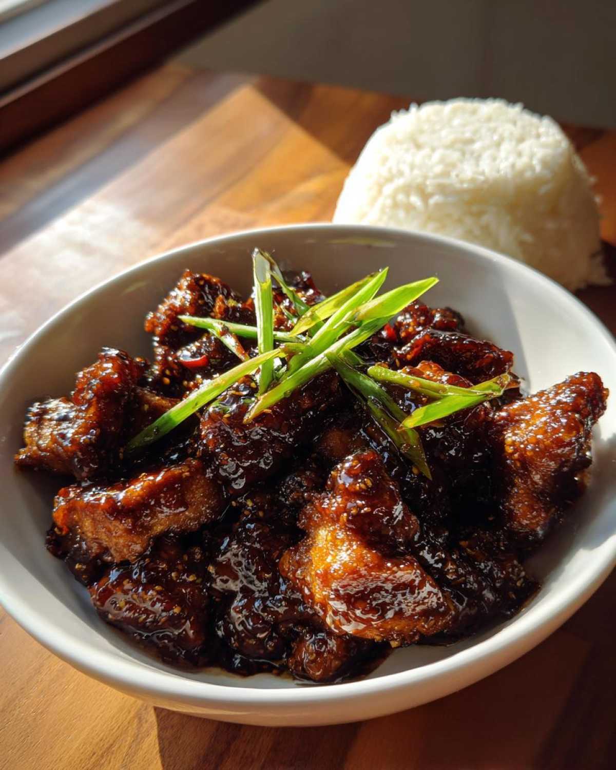 Close-up of Sticky Teriyaki Chicken coated in dark glaze, garnished with green onions, next to a mound of white rice.