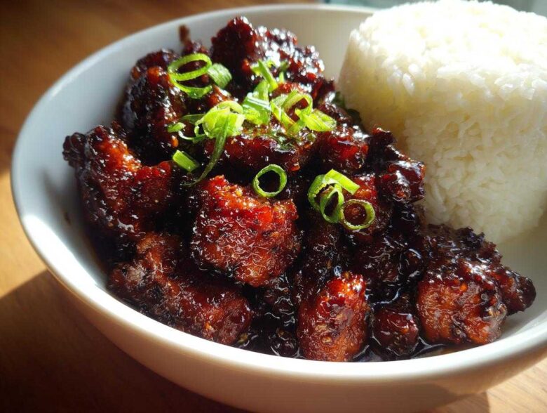 Close-up of Sticky Teriyaki Chicken Easy Weeknight Meal coated in dark glaze, served with white rice and green onions.