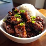 Close-up of Sticky Teriyaki Chicken pieces coated in dark glaze, garnished with green onions, served next to white rice.