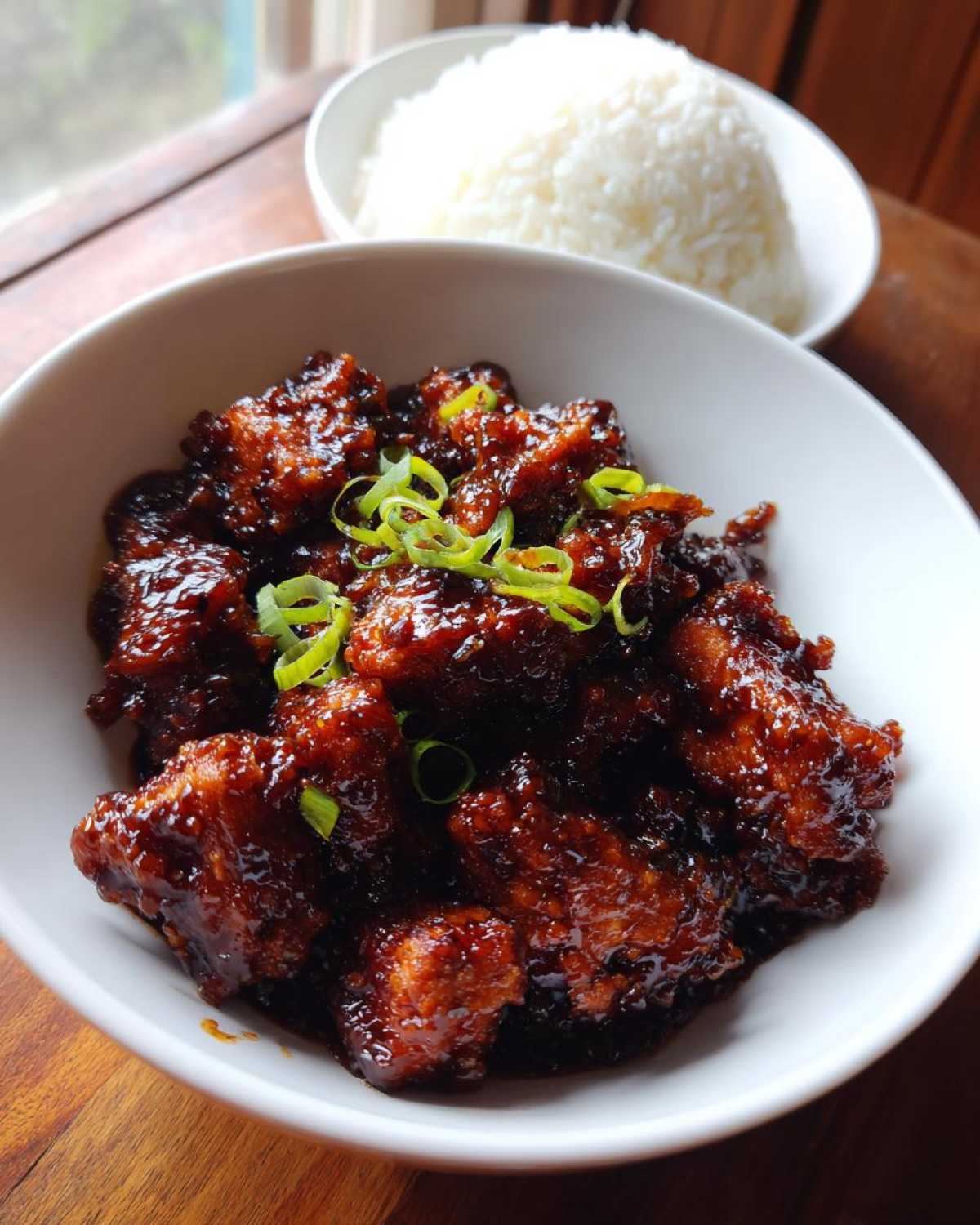 Close-up of Sticky Teriyaki Chicken coated in dark glaze, garnished with green onions, served with a side of white rice.
