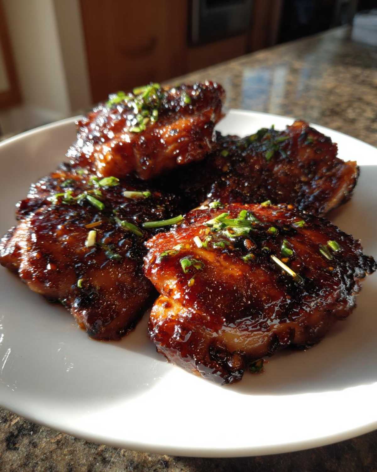 Four pieces of glazed Sticky Teriyaki Chicken Thighs, glistening with sauce and topped with chopped green onions.