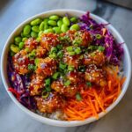 Close-up of a Sweet Chili Chicken Bowl with crispy chicken pieces glazed in sauce, topped with sesame seeds and green onions.