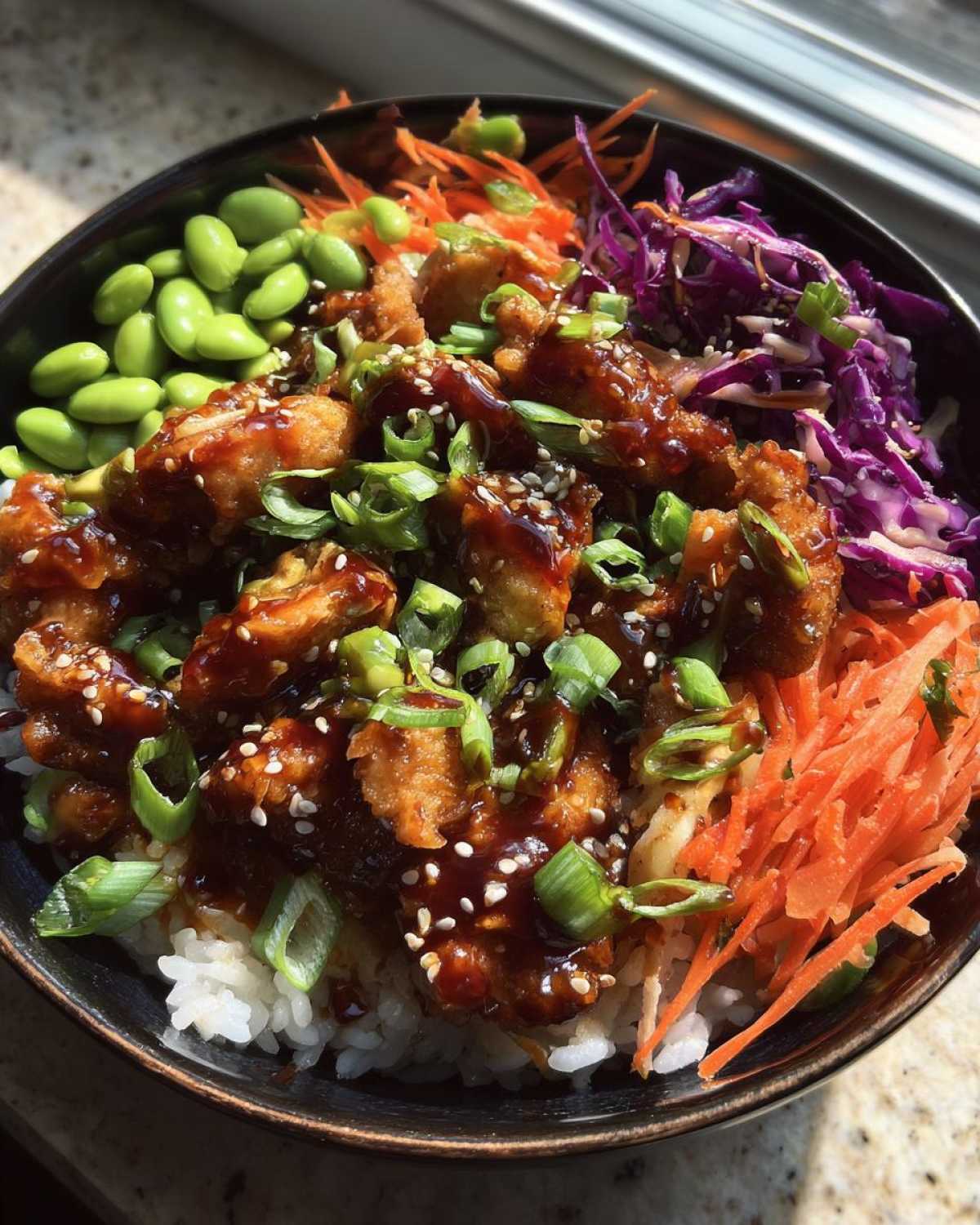 Close-up of a Sweet Chili Chicken Bowl featuring glazed chicken over rice, topped with edamame, shredded carrots, red cabbage, and green onions.