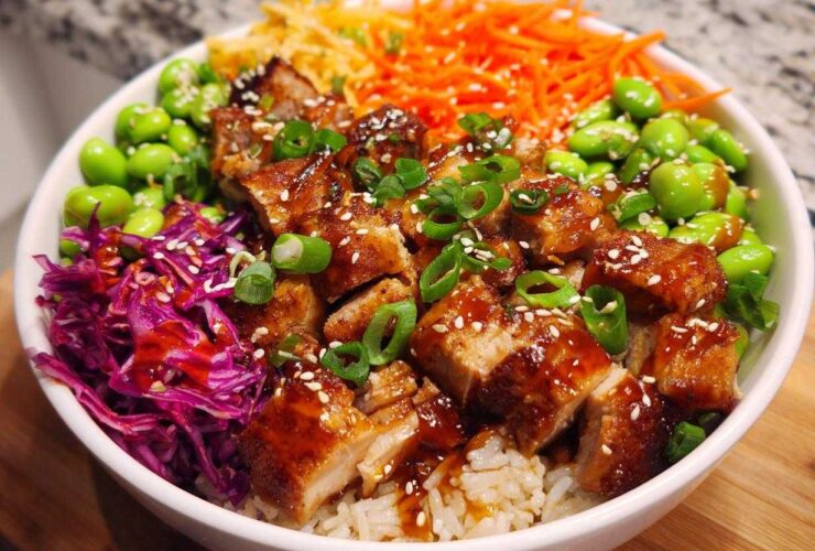 Close-up of a Sweet Chili Chicken Bowl featuring glazed chicken pieces over rice, topped with edamame, shredded carrots, and red cabbage.
