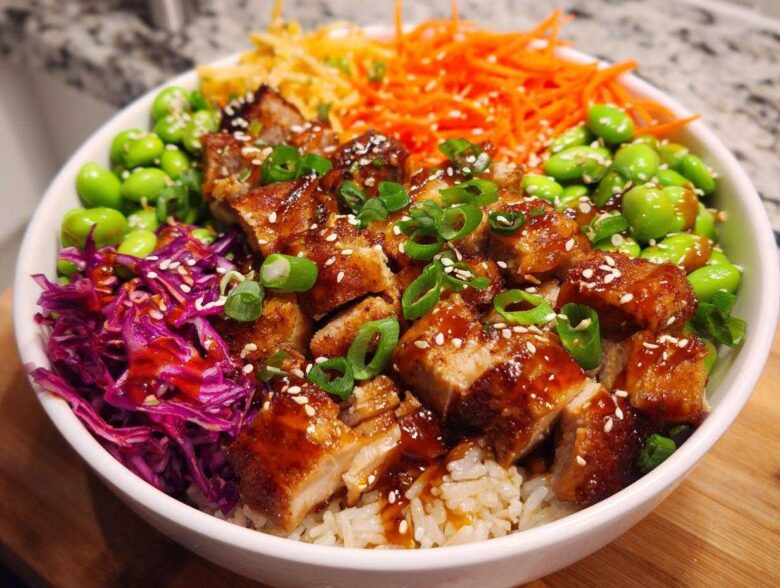 Close-up of a Sweet Chili Chicken Bowl featuring glazed chicken pieces over rice, topped with edamame, shredded carrots, and red cabbage.