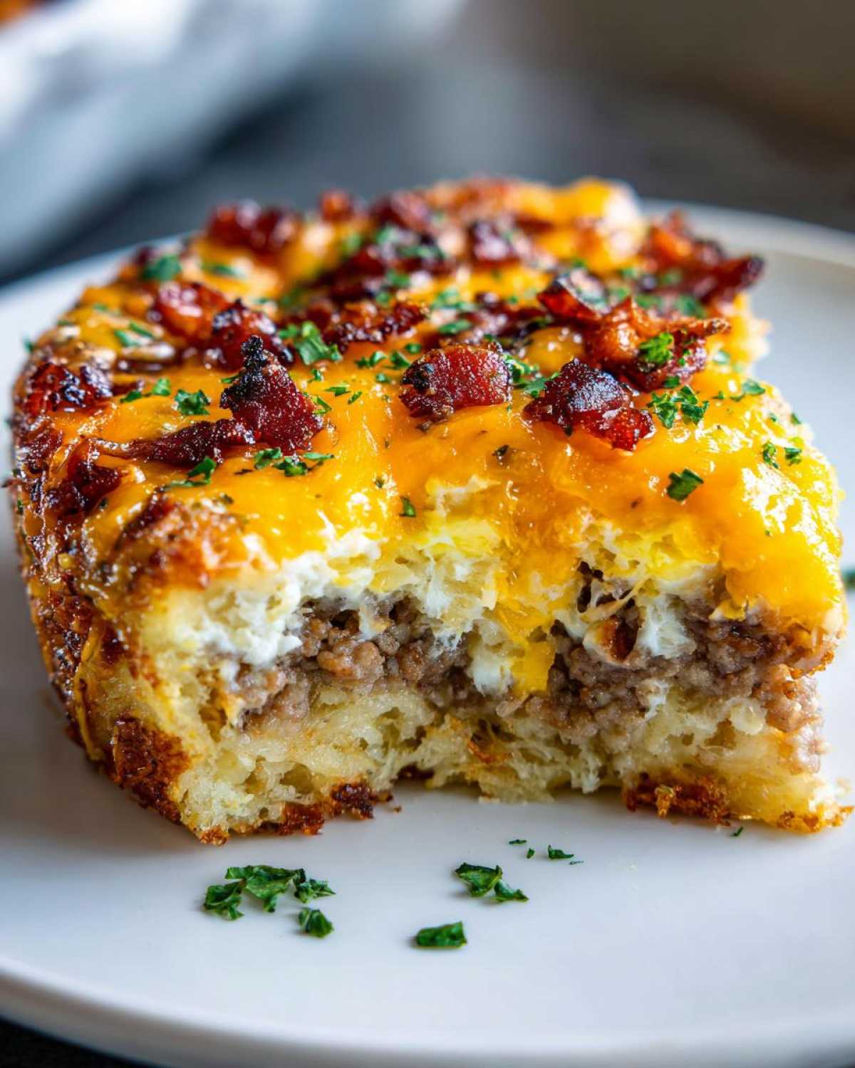 A close-up, bitten slice of Tater Tot Breakfast Casserole topped with melted cheddar cheese and bacon bits.