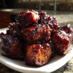 A close-up of glistening, dark-glazed Bbq Chicken Bites piled high on a small white serving dish.