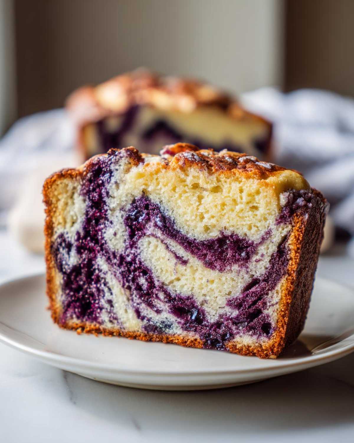 Close-up of a thick slice of Blueberry Cream Cheese Bread Loaf showing a beautiful purple blueberry swirl in the yellow cake.