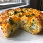 A close-up of a slice removed from a baked Cheesy Cauliflower Broccoli Casserole, showing melted cheddar cheese and green broccoli florets.