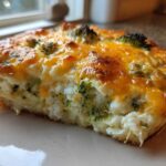 A close-up of a baked slice of Cheesy Cauliflower Broccoli Casserole with melted, golden-brown cheese topping.