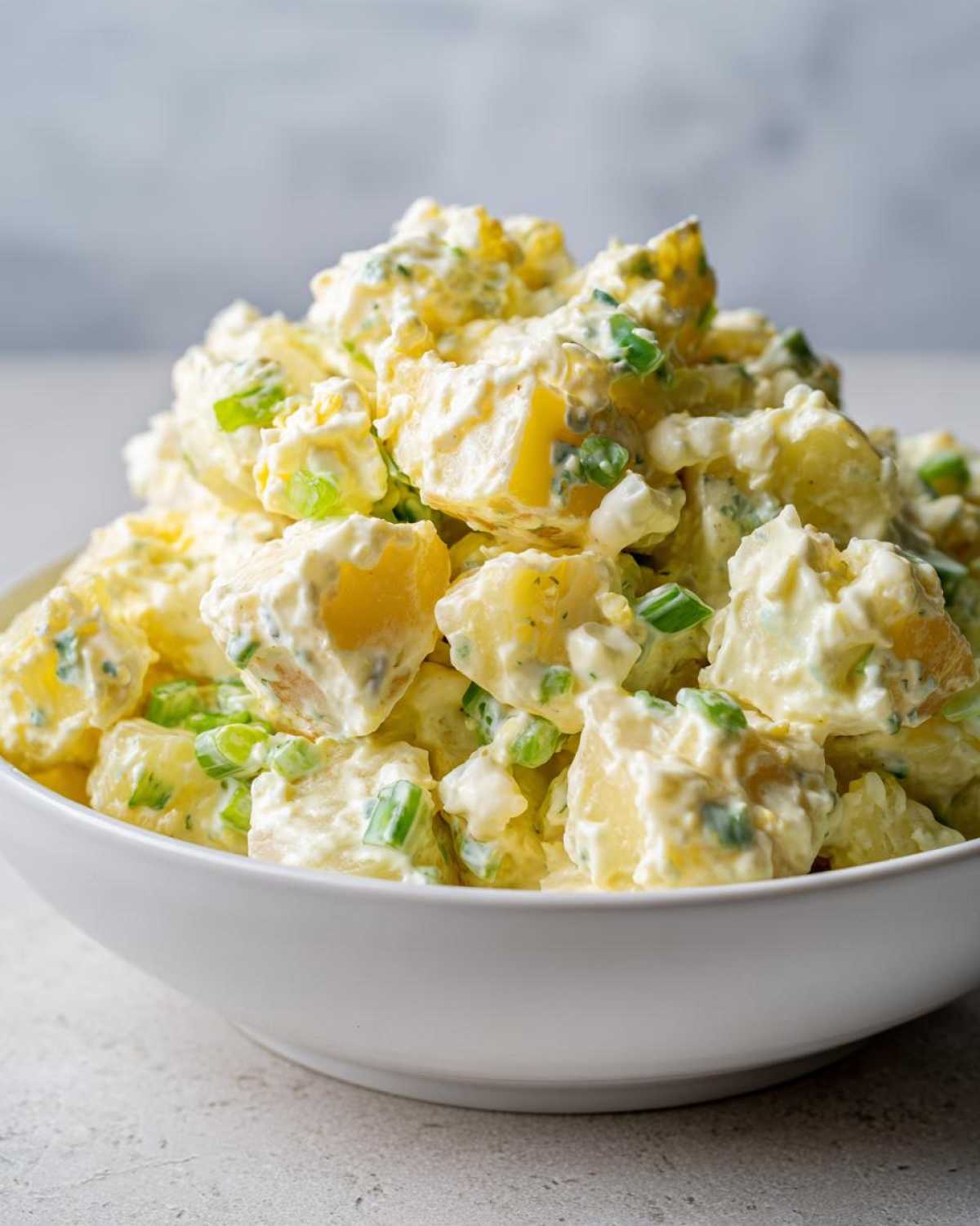 Close-up of a white bowl overflowing with creamy Chick-fil-A Potato Salad chunks and green onions.