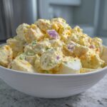 A large white bowl filled with creamy Chick-fil-A Potato Salad featuring chunks of potato, egg, and red onion.