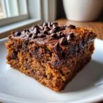 A moist, square slice of Chocolate Chip Banana Bars topped with melted chocolate chips, served on a white plate.
