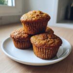 A stack of four golden brown Cottage Cheese Banana Muffins resting on a small white plate.