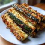 A stack of golden brown, breaded Air Fryer Zucchini sticks served on a white plate.