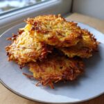 A stack of four golden brown, crispy German Potato Pancakes piled on a light gray plate near a window.