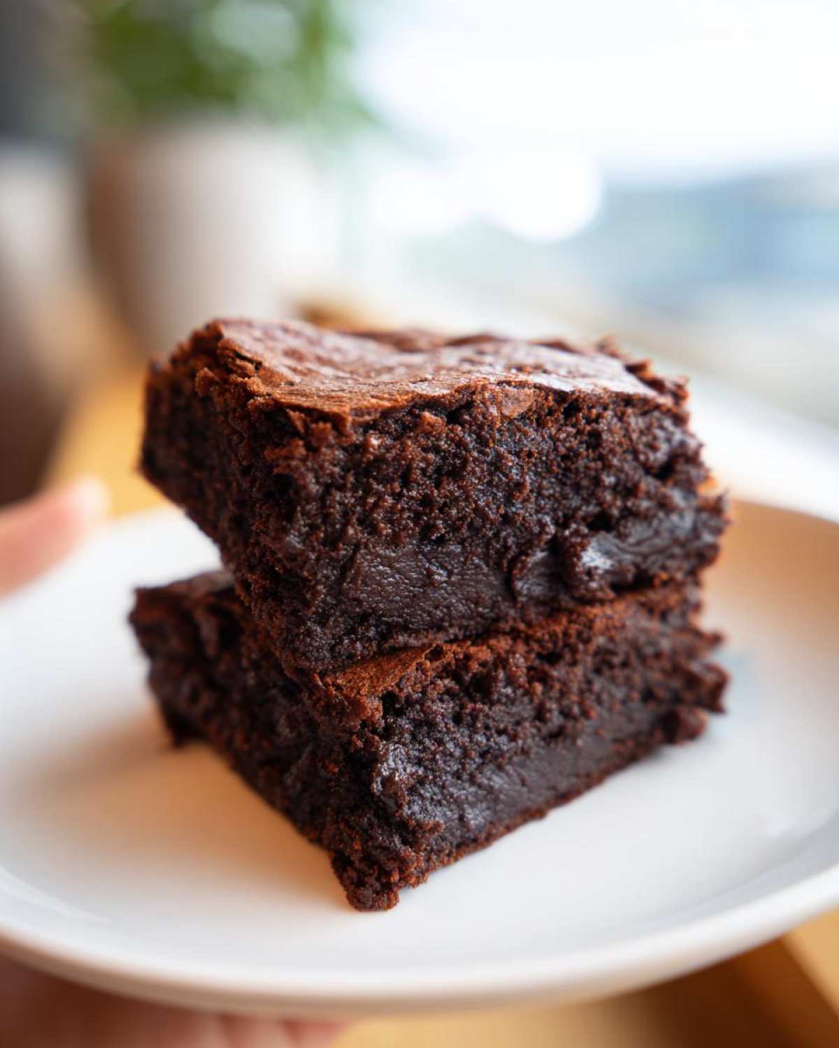 Two rich, fudgy squares of Protein Brownie stacked on a white plate, showing a moist interior.