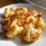 Close-up of golden brown, caramelized Garlic Butter Roasted Cauliflower florets on a white plate.