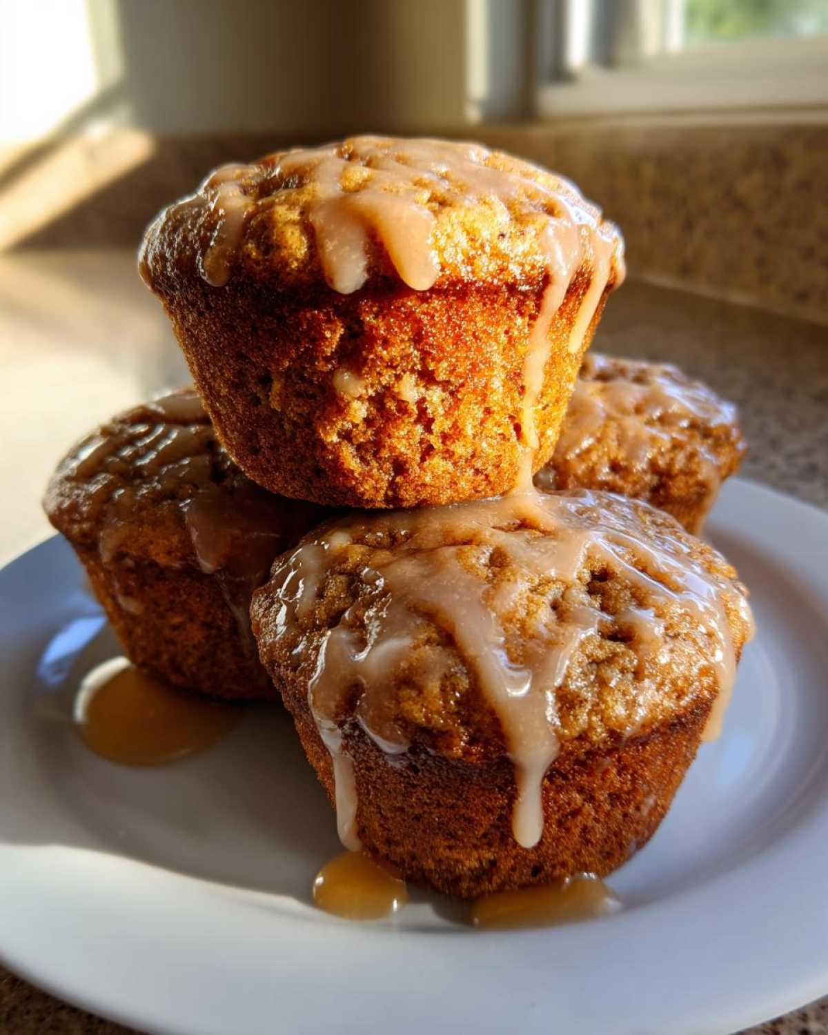 Three moist Vanilla Chai Muffins stacked on a white plate, generously drizzled with a light brown glaze.