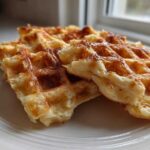 Close-up of light, fluffy Belgian Waffles with caramelized edges on a white plate.