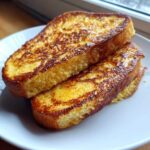 Two thick slices of golden brown French Toast stacked on a white plate.