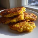 A stack of four crispy, golden brown German Potato Pancakes resting on a white plate near a sunlit window.