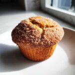 A close-up of a freshly baked Greek Yogurt Cinnamon Muffin topped with sparkling cinnamon sugar.