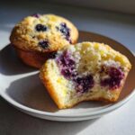 Close-up of a half-eaten Lemon Blueberry Muffin showing the moist crumb and burst blueberries inside.