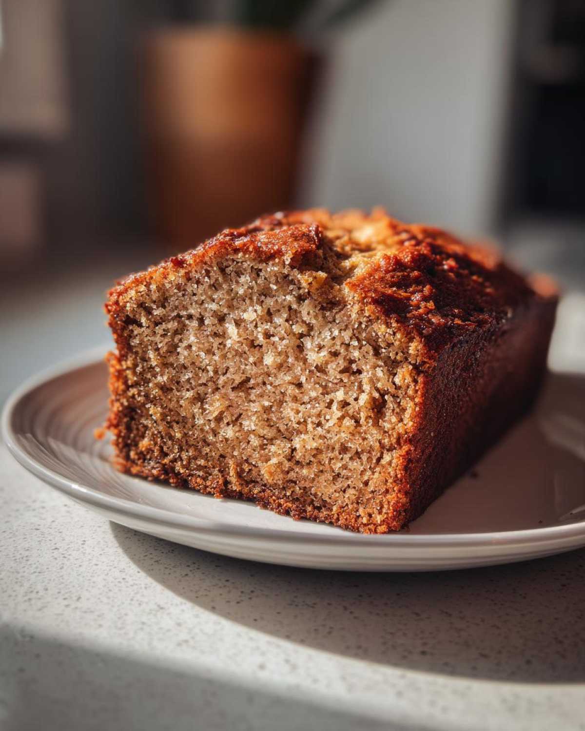 A close-up shot of a thick slice of moist Banana Bread with a golden-brown crust, sitting on a small plate.