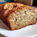 Close-up of two slices of moist, golden-brown Banana Bread served on a white plate.