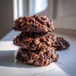 A close-up stack of three moist No-Bake Chocolate Oatmeal Cookies on a white marble surface.