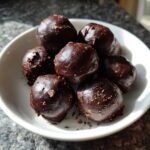 A close-up of several rich, dark chocolate-coated No-Bake Oreo Bites stacked in a small white bowl.