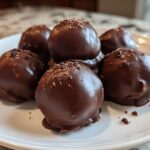 A plate holding six rich, chocolate-covered No-Bake Oreo Bites, sprinkled with dark crumbs.