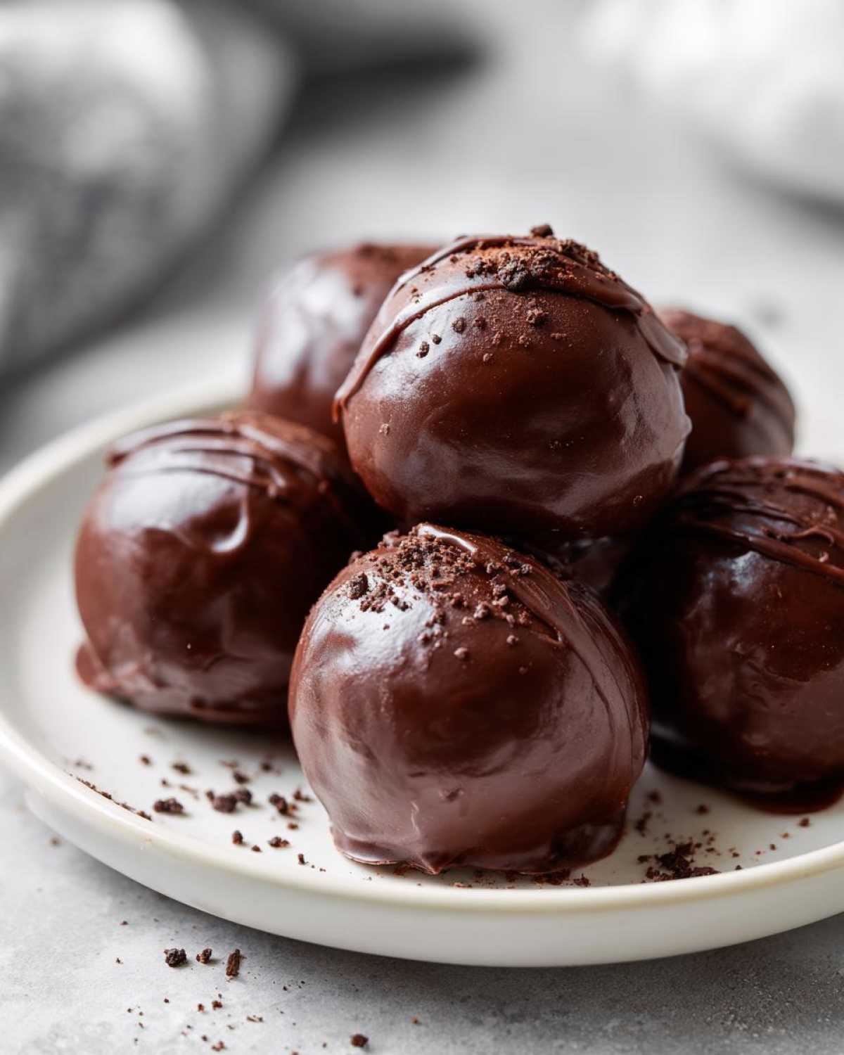 Close-up of several rich, chocolate-covered No-Bake Oreo Bites stacked on a white plate.