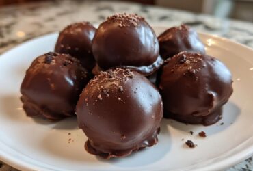 A plate holding six rich, chocolate-covered No-Bake Oreo Bites, sprinkled with dark crumbs.