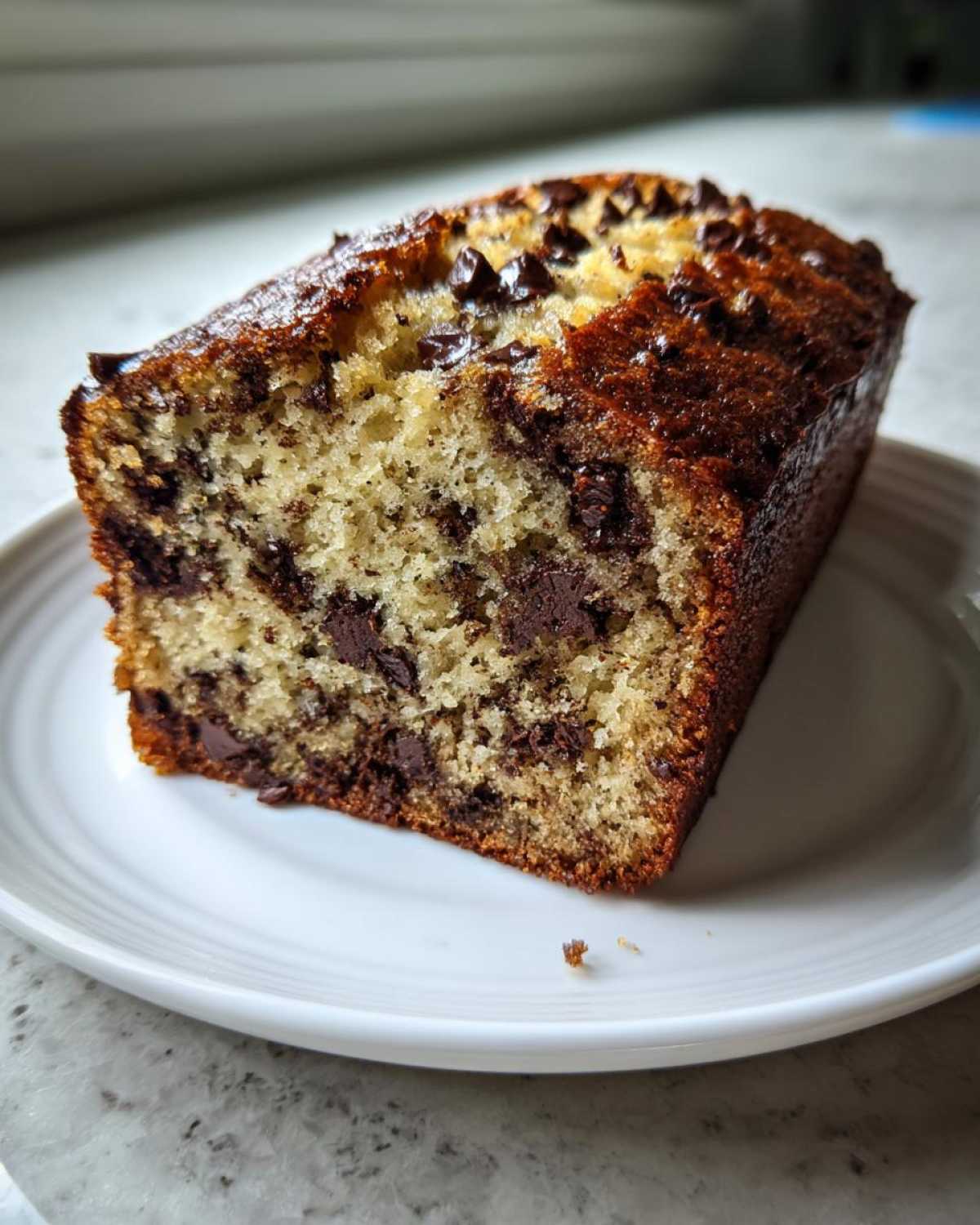 A close-up of a moist slice of One-Bowl Banana Bread with Chocolate Chips on a white plate.