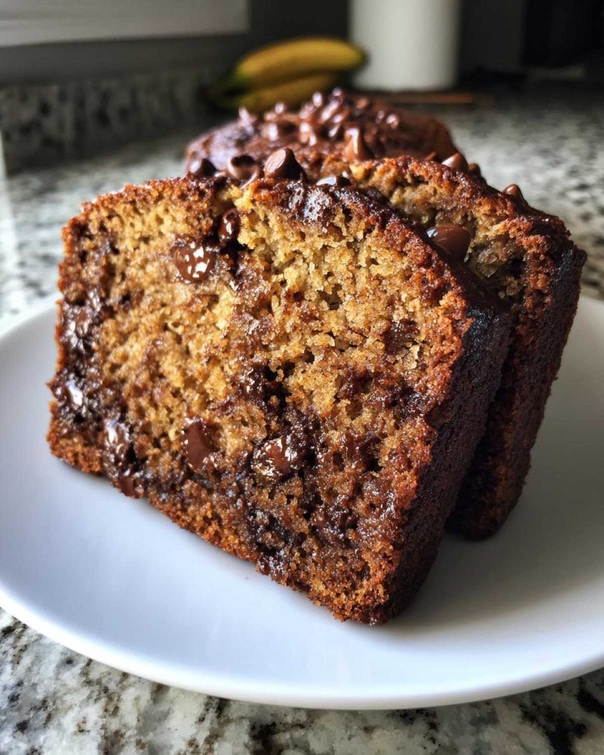Two thick slices of moist One-Bowl Banana Bread with Chocolate Chips served on a white plate.