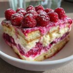 A decadent slice of Raspberry Tiramisu showing layers of ladyfingers, cream, and fruit, topped with fresh raspberries and powdered sugar.