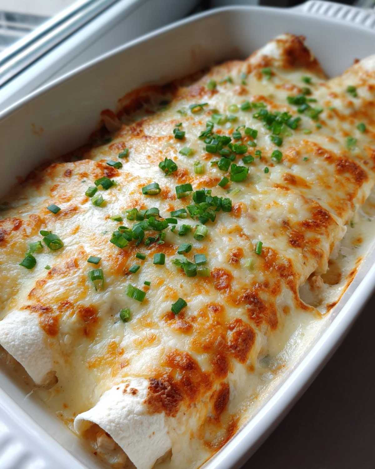 Close-up of baked Sour Cream Chicken Enchiladas covered in bubbly, browned cheese and topped with fresh green onions.