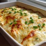 Close-up of baked Sour Cream Chicken Enchiladas covered in bubbly, melted white cheese and green onions.
