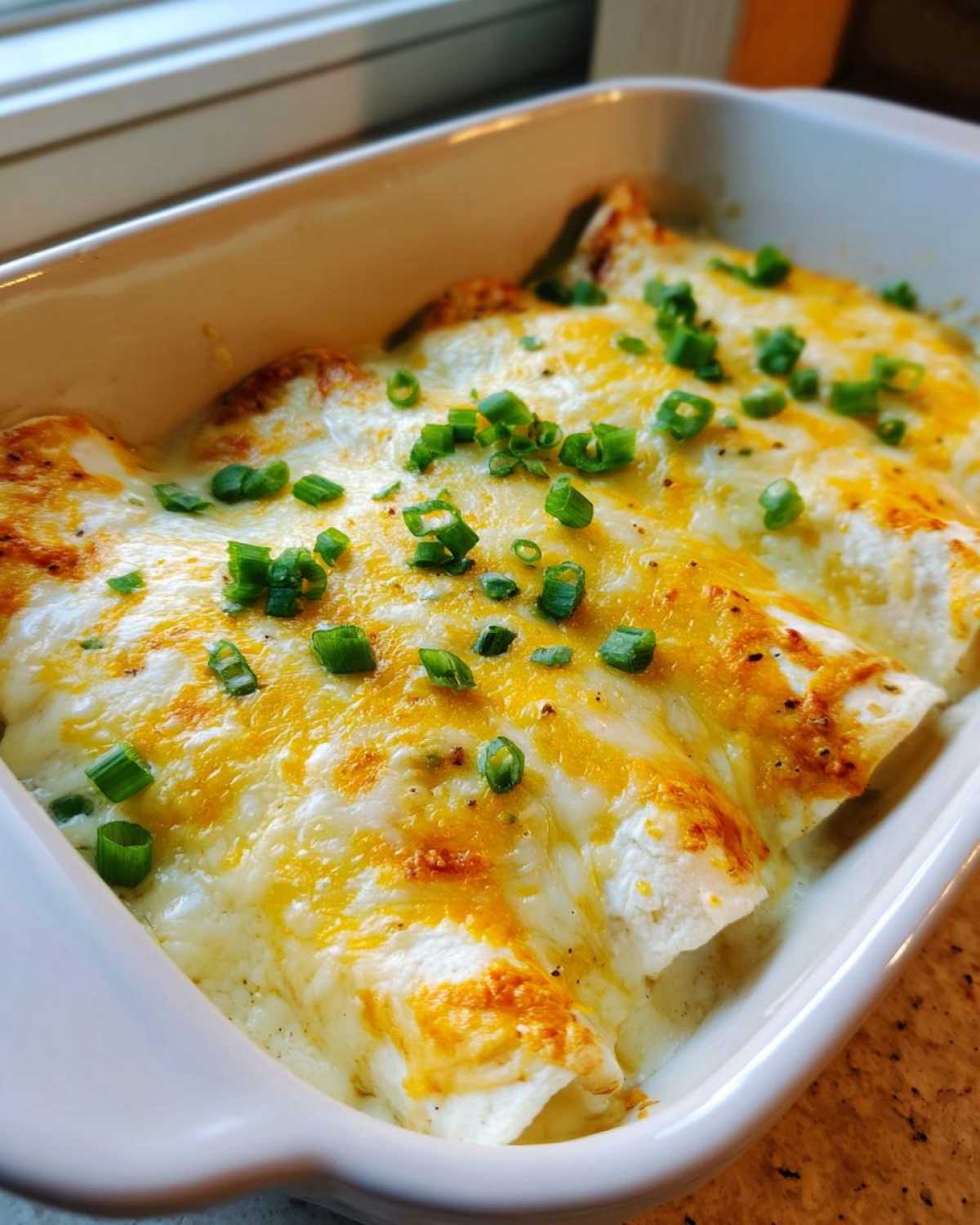 Close-up of baked Sour Cream Chicken Enchiladas covered in melted white and cheddar cheese and topped with green onions.