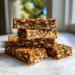 A stack of four dense, chewy High-Protein Energy Bars packed with visible seeds and grains.