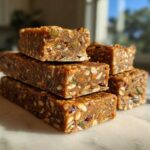A stack of homemade, dense High-Protein Energy Bars packed with visible nuts and seeds, set against a bright, sunlit background.