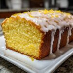 A close-up of a freshly baked Starbucks Lemon Loaf, featuring a thick, dripping lemon glaze and bright zest topping.