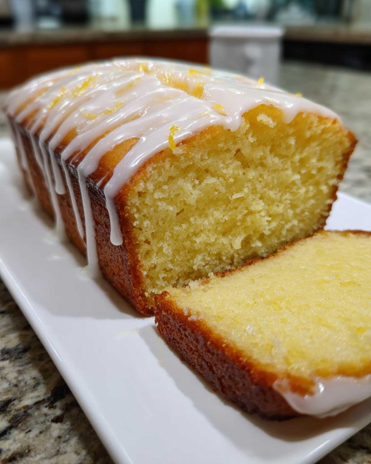 A moist Starbucks Lemon Loaf, drizzled with white icing and topped with lemon zest, with one slice cut.