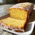 A close-up of a moist Starbucks Lemon Loaf, sliced to show the crumb, topped with white glaze and lemon zest.