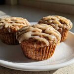 Three moist Vanilla Chai Muffins topped with a creamy glaze, resting on a white plate in natural sunlight.