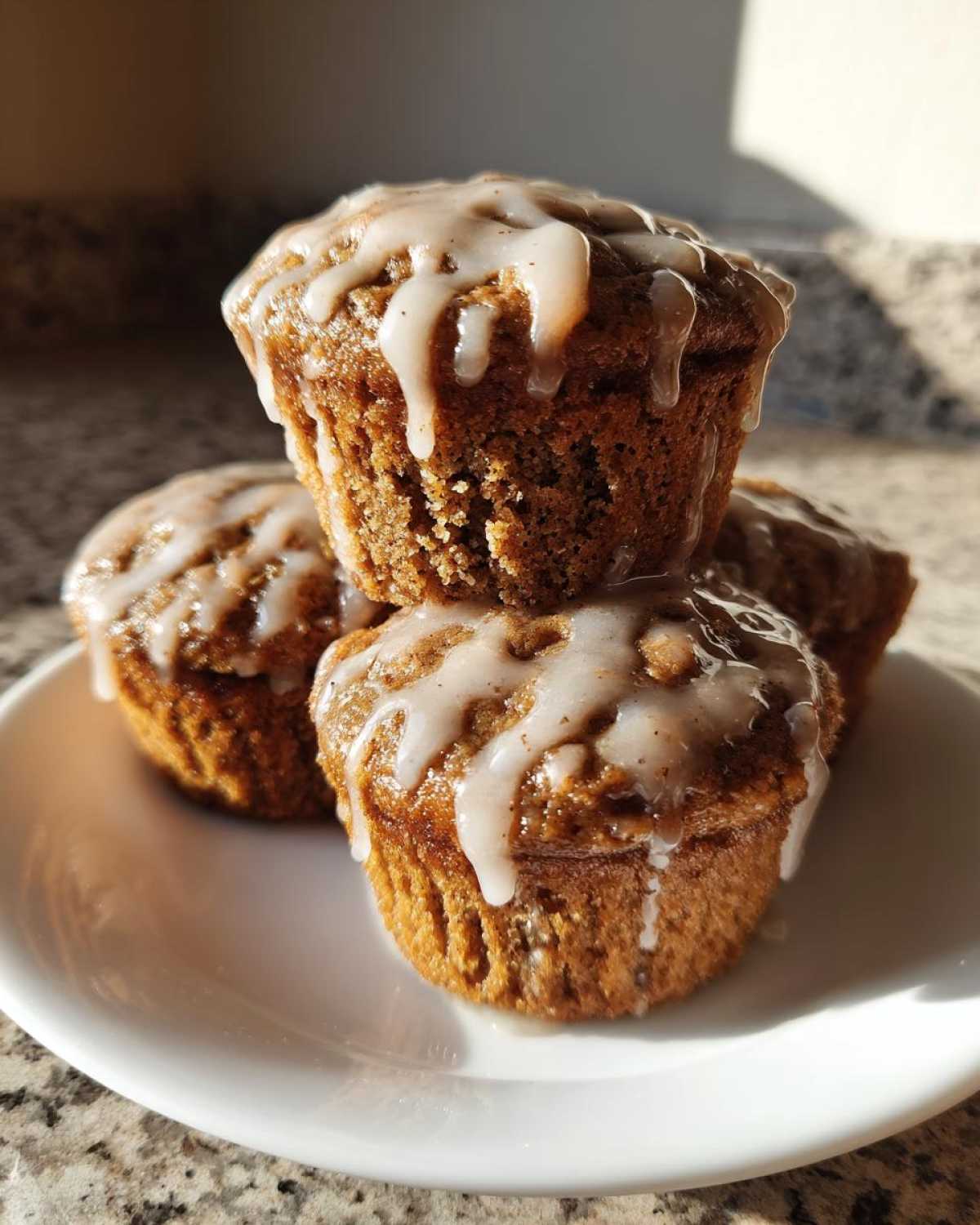 A stack of three delicious Vanilla Chai Muffins topped with a thick, dripping vanilla glaze.