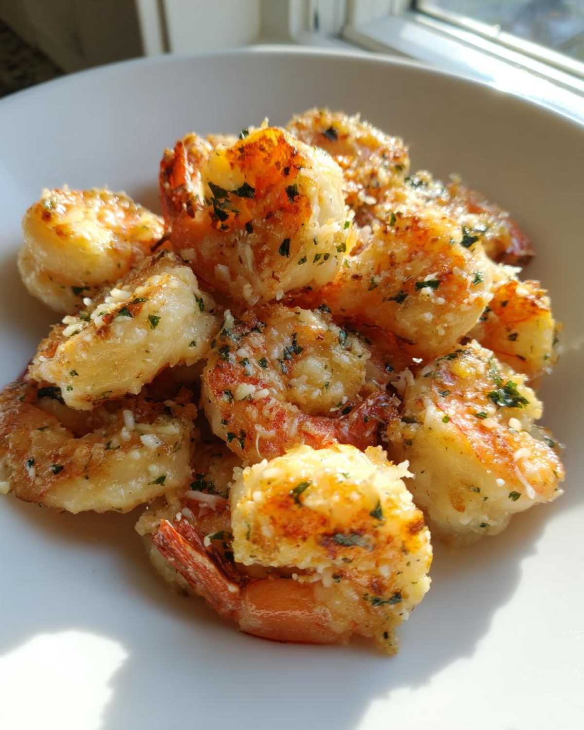 Close-up of golden, cooked Air Fryer Garlic Parmesan Shrimp topped with grated cheese and parsley in a white bowl.